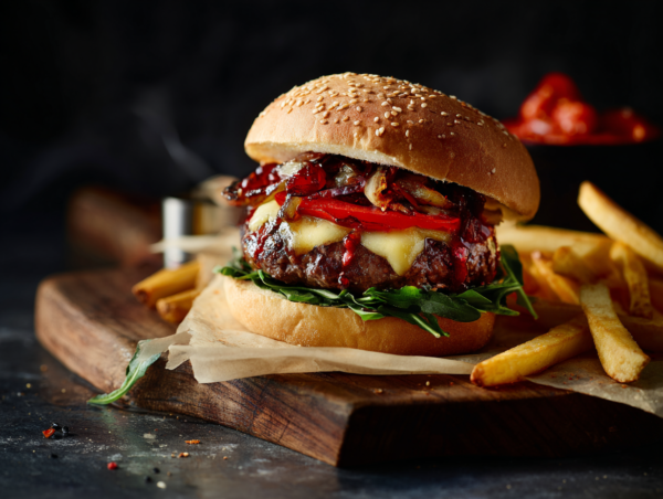 Beef Burger served with lettuce, grilled vegetables, and chips on a wooden board against a dark background.