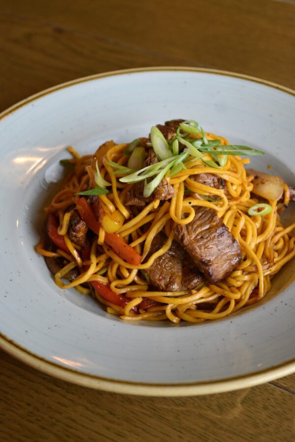 Beef Stir Fry Mix served with noodles, red peppers, and spring onions on a white plate.