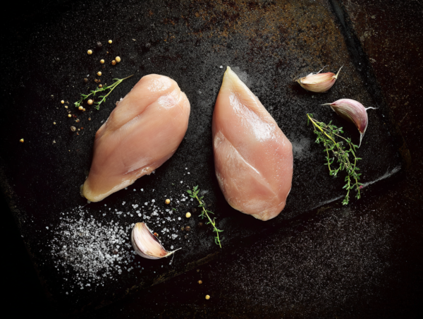 Free-range chicken breast with garlic, salt, peppercorns, and thyme on a dark surface.