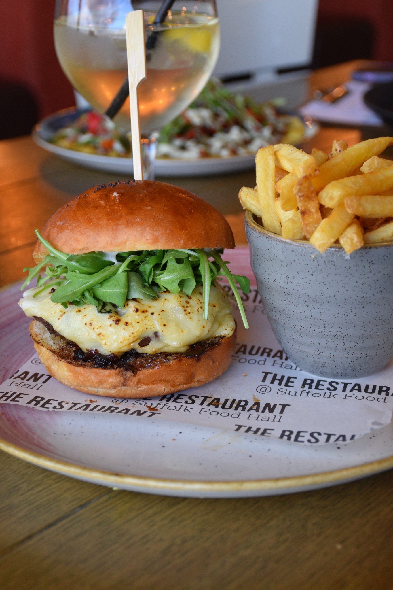 Cheeseburger with rocket in a bap served with a cup of chips on a plate.