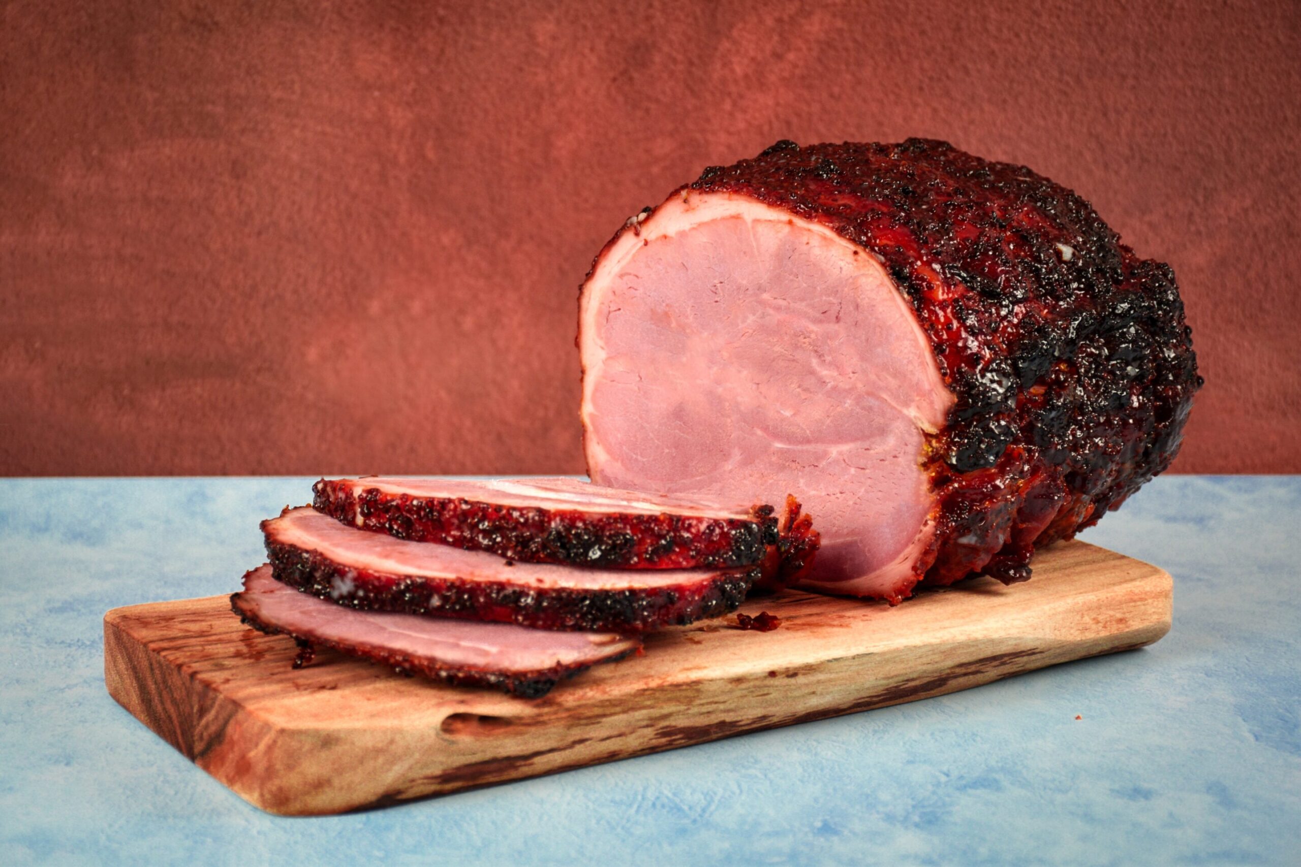 Our Own Traditional Ham, sliced and served on a wooden chopping board with a blue and brown backdrop.