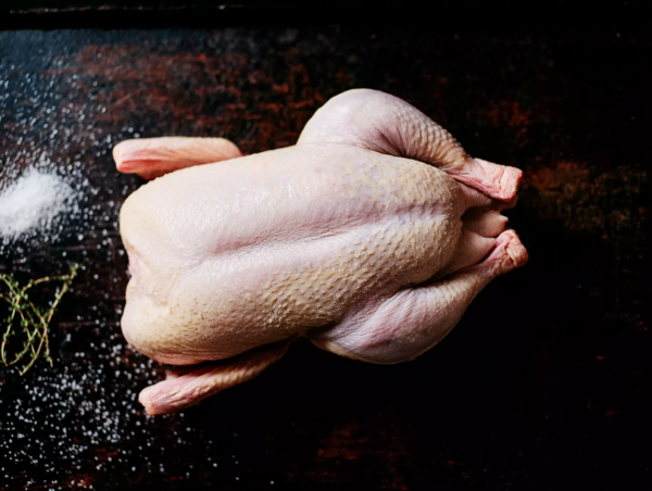 Whole duck on a dark surface with salt and herbs scattered nearby.