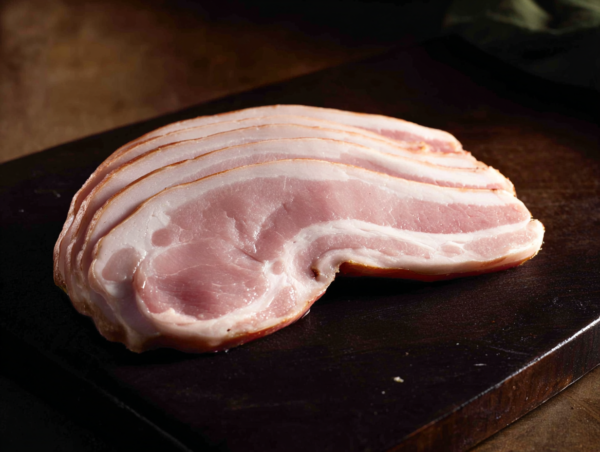 Several rashers of Green Back Bacon are stacked on a dark wooden chopping board.