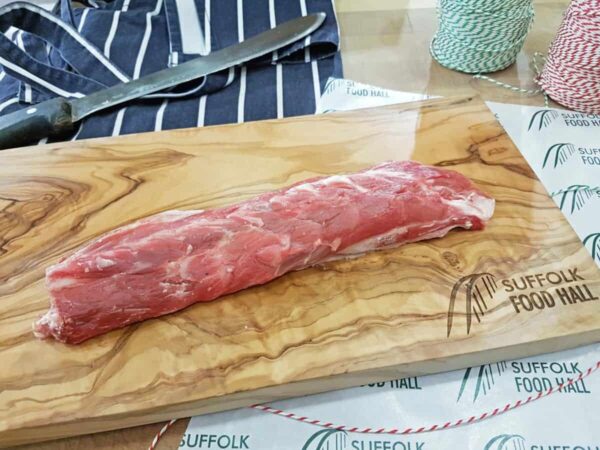 Lamb neck fillet on a wooden chopping board with a knife and string in the background.