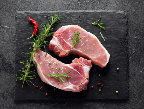 Two Pork Sirloin Steaks on black slate with rosemary, red chilli, and peppercorns.
