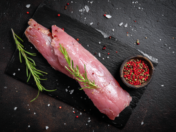 Pork fillet displayed on a slate board with rosemary and a bowl of mixed peppercorns.