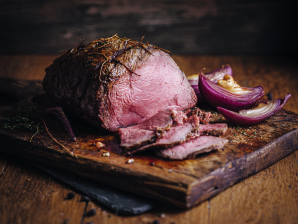 Cooked chuck roast, sliced and served on a wooden board with roasted red onion wedges.
