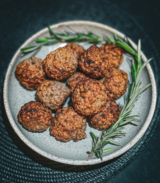Sage, Onion & Sausage Meat Stuffing Balls garnished with rosemary on a dark surface.