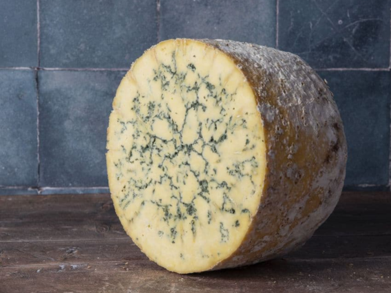 A wheel of Cropwell Bishop Stilton sits on a wooden surface with a tiled background.