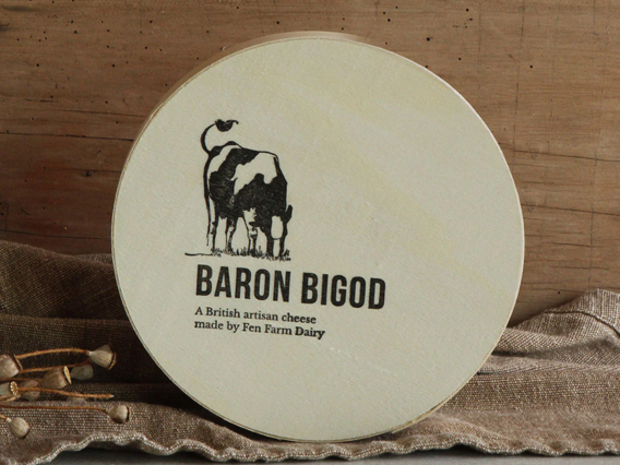 Round wooden box of Baron Bigod cheese with a cow illustration, set on a brown cloth background.