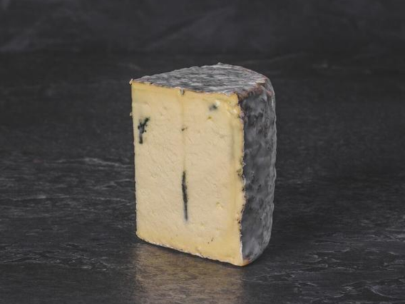 A wedge of Suffolk Blue cheese with a greyish rind and blue-green veins sits on a dark surface.