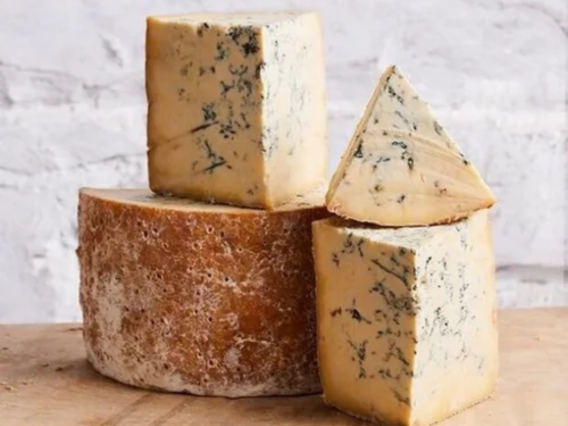 Three pieces of Colston Bassett Stilton, including wedges and a wheel, on a wooden surface.