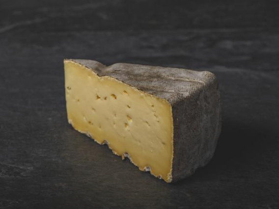 Suffolk Gold, a semi-soft yellow cheese with a natural greyish-brown rind, displayed on a dark surface.