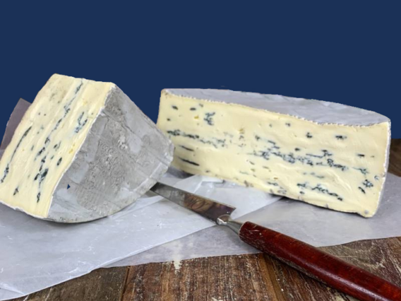 Two wedges of Montagnolo Affline blue cheese on greaseproof paper with a knife, set on a wooden surface.