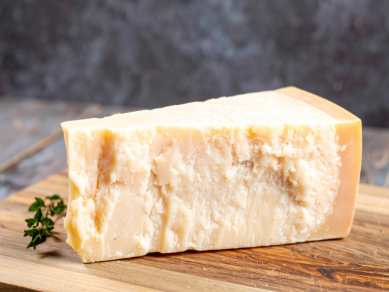 A wedge of Parmigiano Reggiano Parmesan sits on a wooden board with a sprig of herbs beside it.