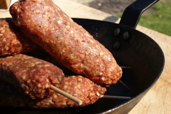 Lamb Kofta Kebab skewers in a black pan on a wooden surface, ready to be cooked.