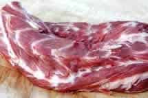 Lamb neck fillet with visible marbling of fat on a light-coloured chopping board.