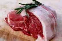A lamb rump with a fat layer, tied with string, and topped with rosemary on a wooden surface.