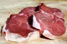 Two raw lamb leg steaks with bone on a light-coloured chopping board.