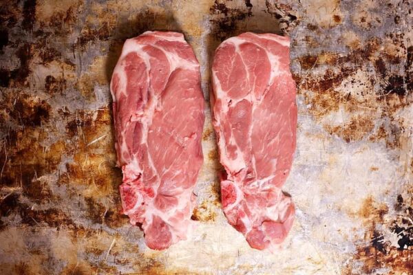 Two raw lamb shoulder steaks placed side by side on a rough, stained metal surface.