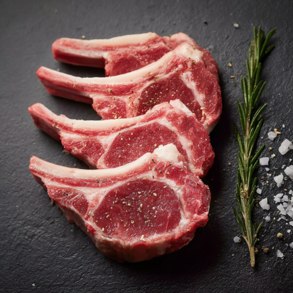 Three Lamb Chop Cutlets with seasoning, rosemary, and coarse salt on a dark slate surface.